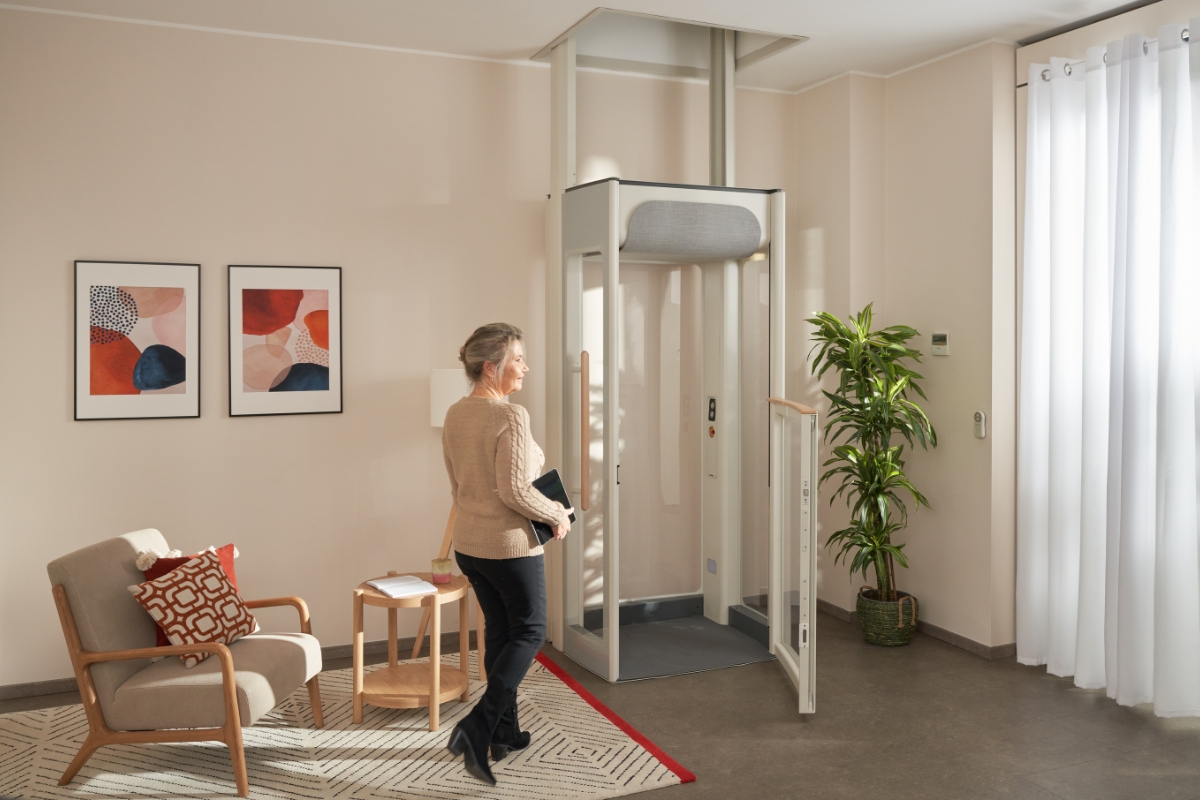 Μεσήλικη γυναίκα χαμογελά καθώς περπατά προς τον ανελκυστήρα Uplifts S2 του σπιτιού της. 